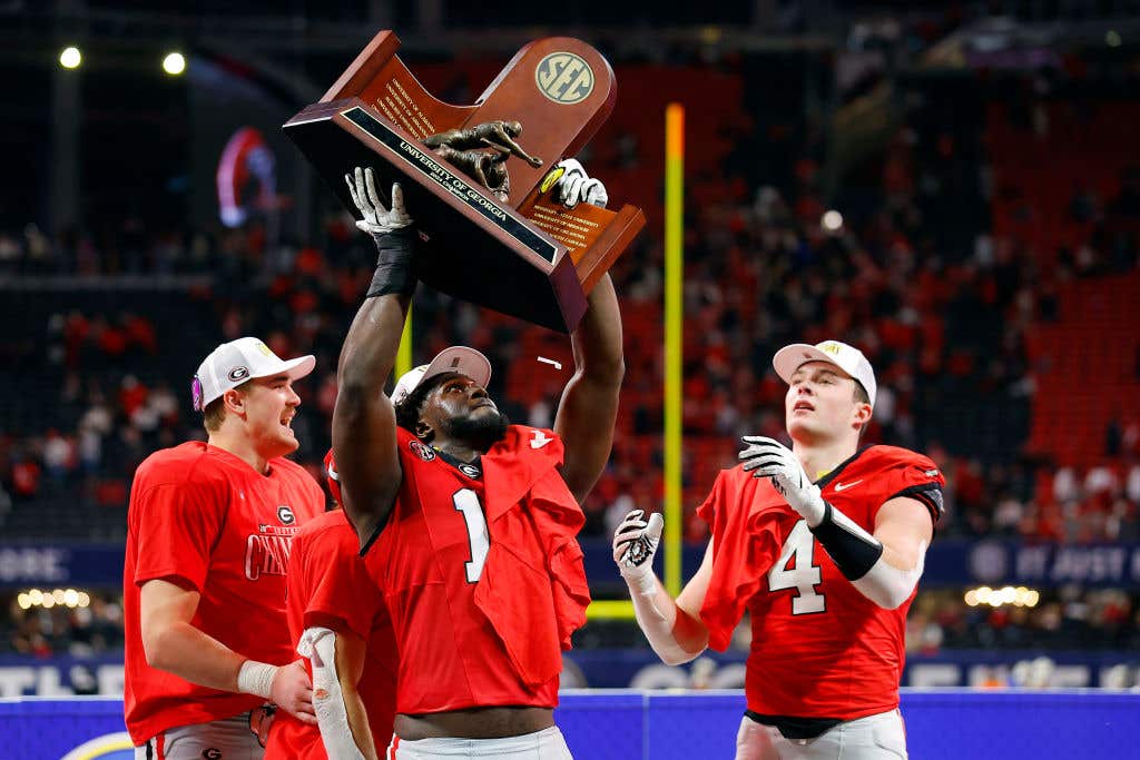 ATLANTA, GEORGIA: Jalon Walker #11 and Oscar Delp #4 of the Georgia Bulldogs celebrate with the trophy after defeating the Texas Longhorns 22-19 in overtime of the 2024 SEC Championship at Mercedes-Benz Stadium on December 07, 2024 in Atlanta, Georgia.