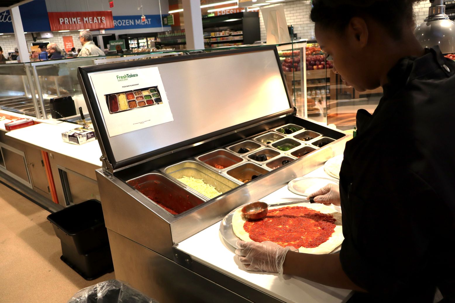 A FreshTake employees prepares a pizza for the store's pizza ovens. Fresh pizza are among the offerings at the new Augusta store.