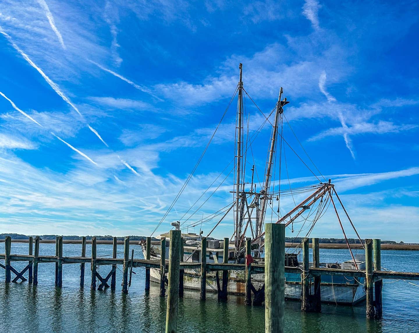 The two sides of Port Royal. A boat sits quietly at the dock while vapor trails from Marine jets stripe the sky.