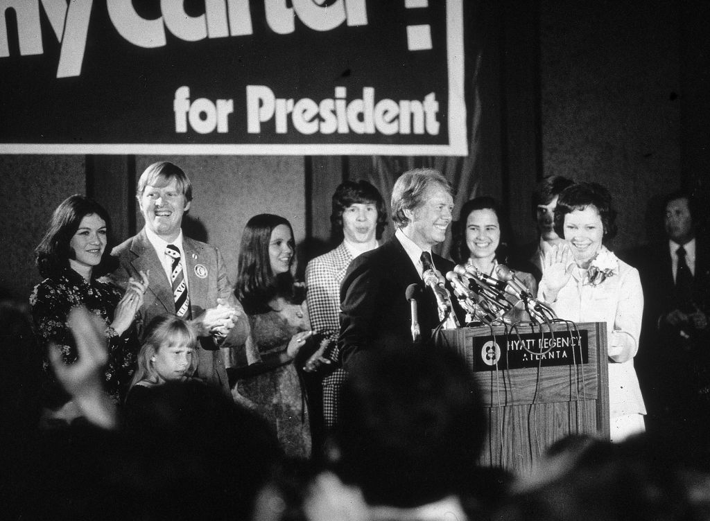 Democratic presidential candidate Jimmy Carter speaks at a podium  while his brother Billy, wife Rosalynn and other family  members applaud on election night, Hyatt Regency Hotel, Atlanta, Georgia, 1976. This is the moment the writer learned what Georgia sounded like.